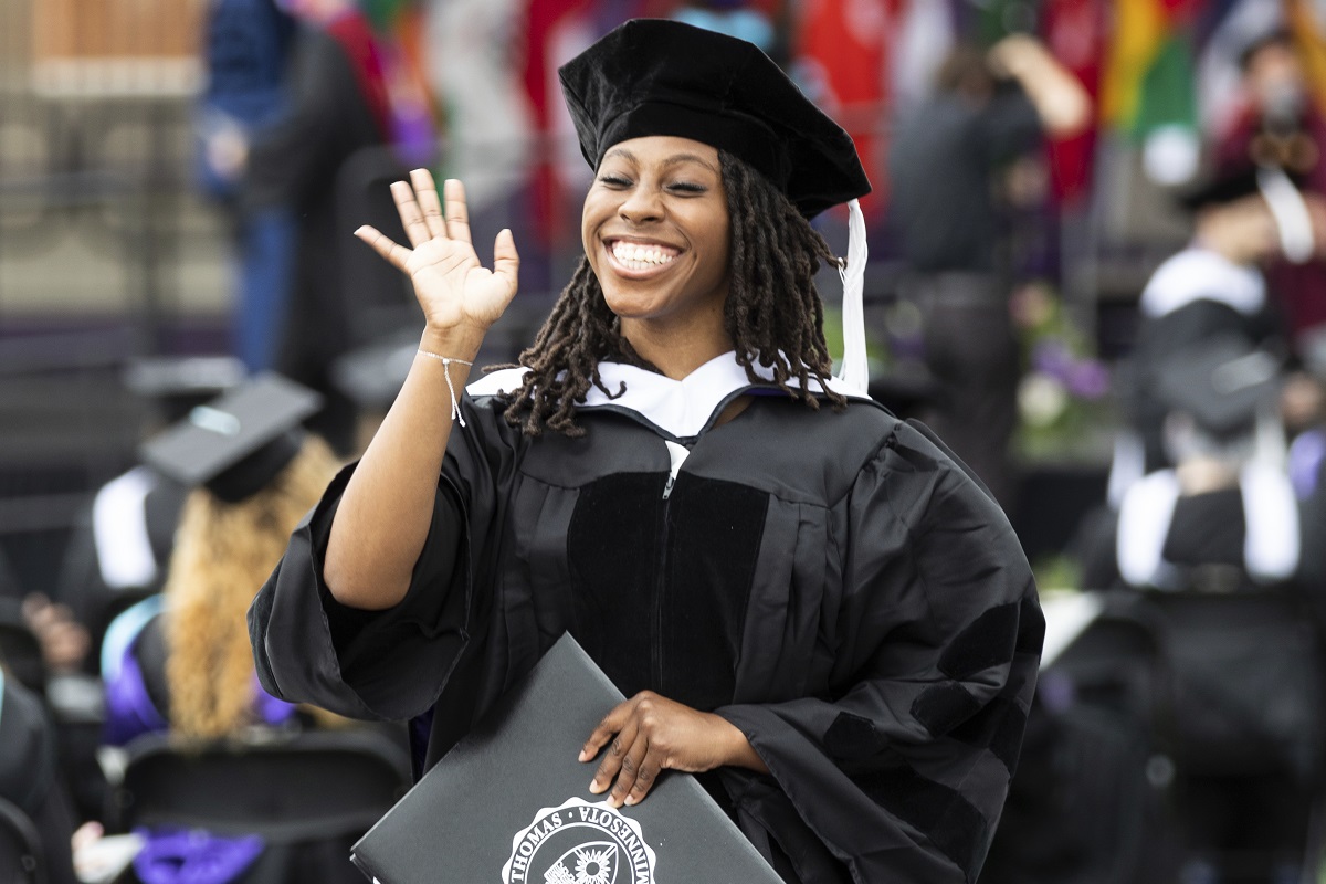 A student smiles and waives after receiving her diploma