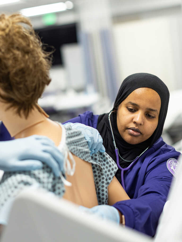 A nursing student works with a simulation mannequin