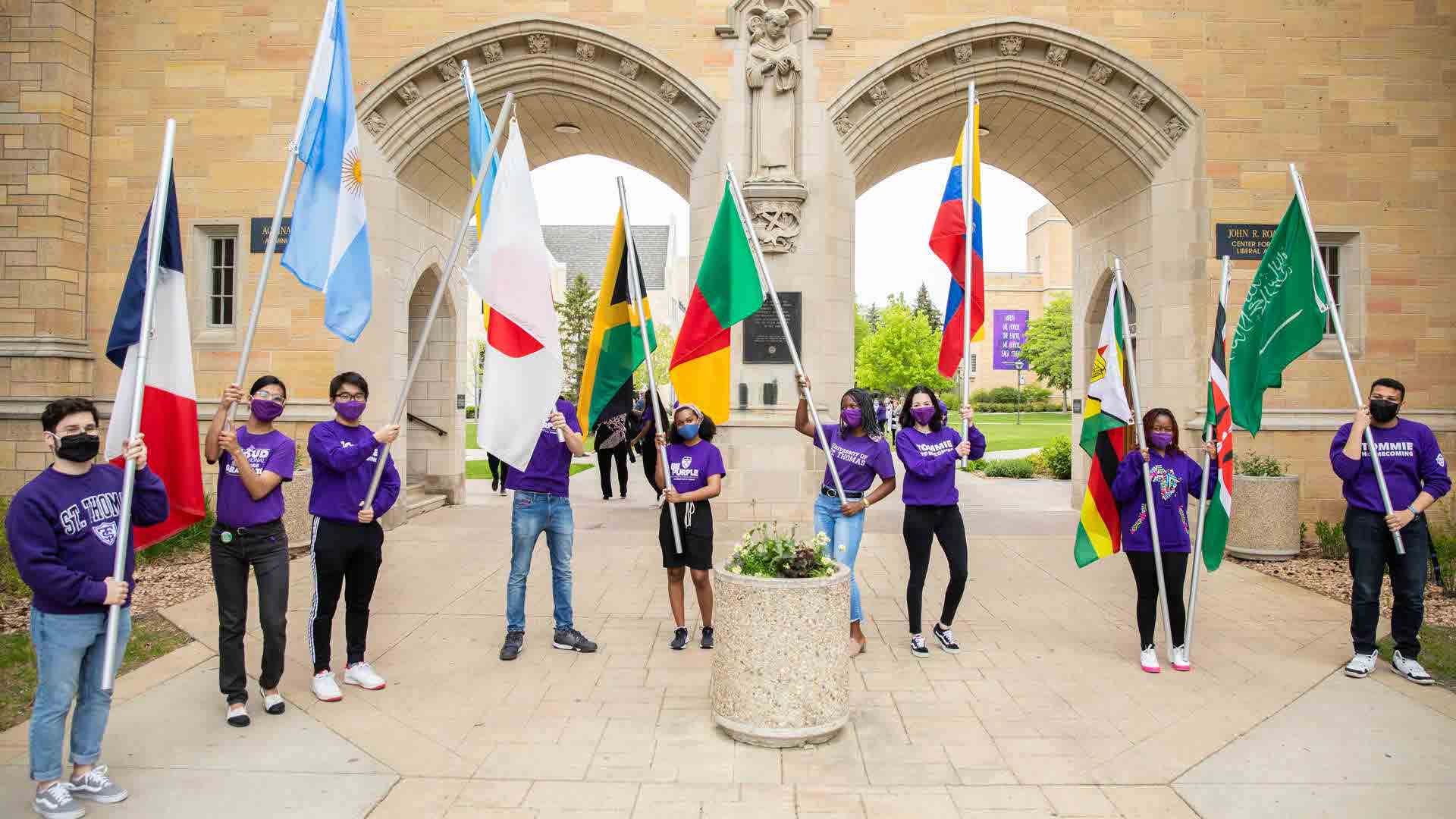international students holding flags in front of the arches