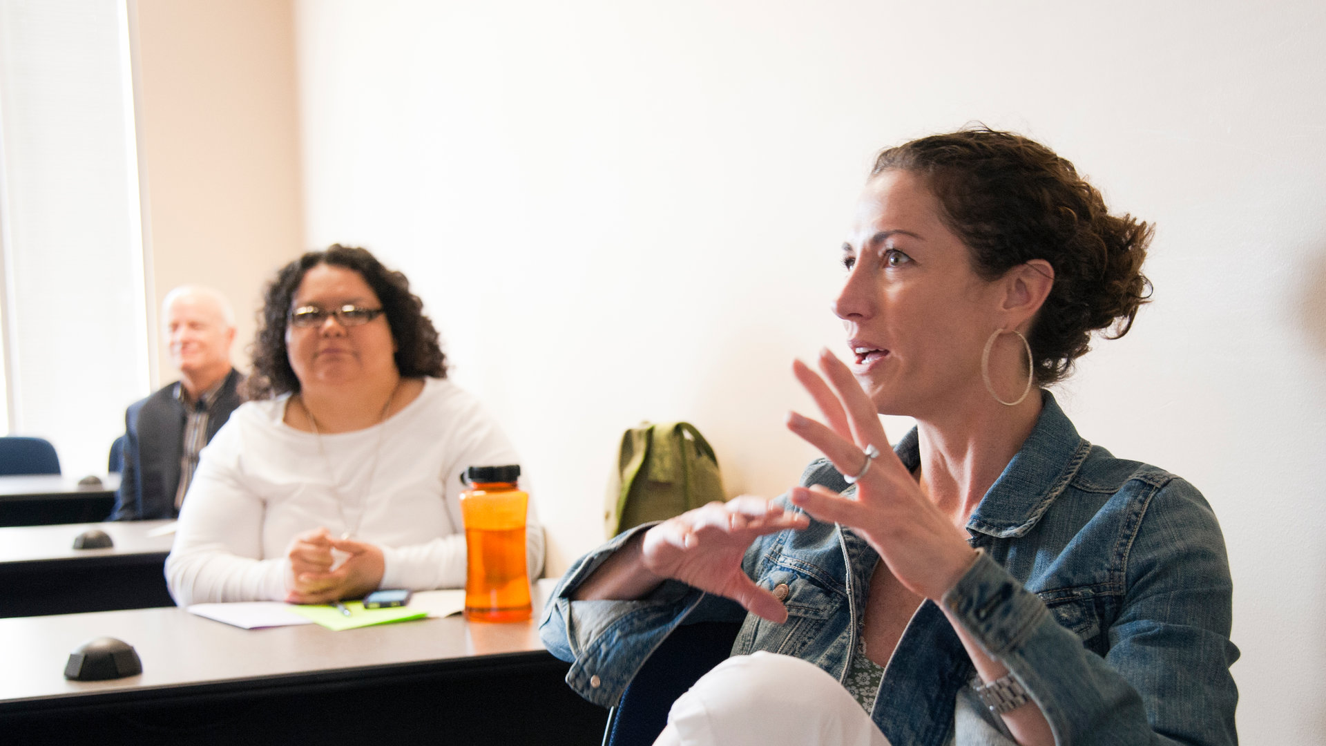 A woman speaks while sitting in a classroom. 