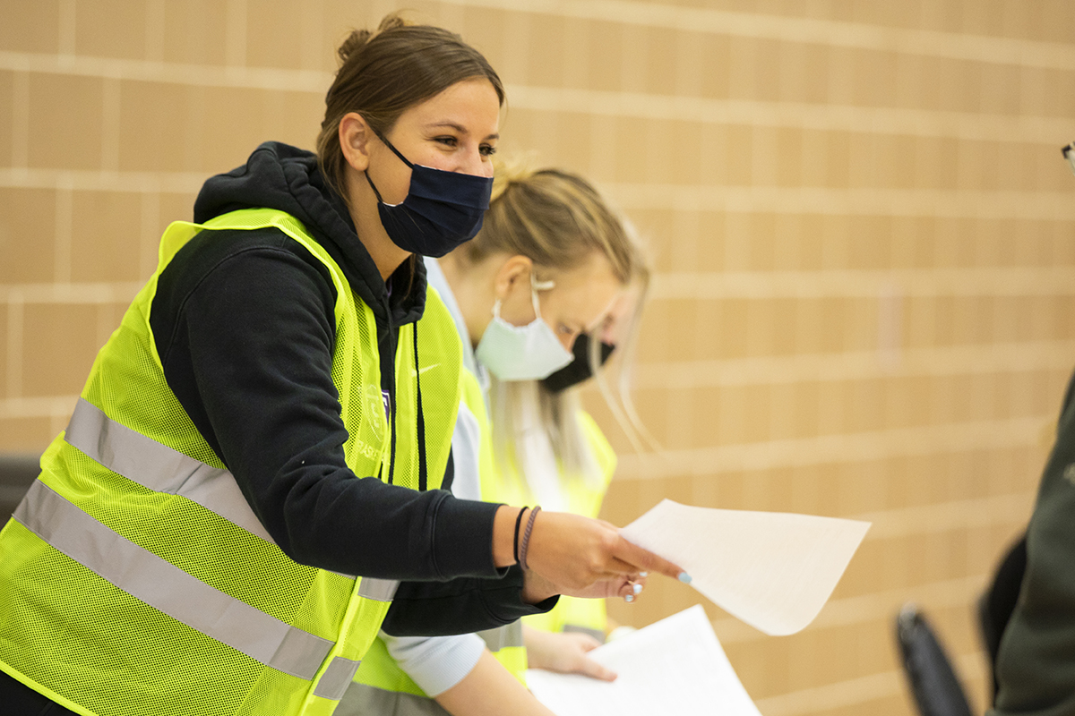 A woman in a mask hands paperwork to a client