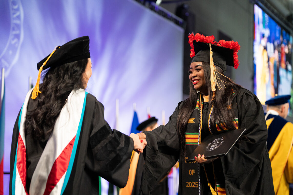 A student shakes hands with the Dean while walking across the stage at commencement