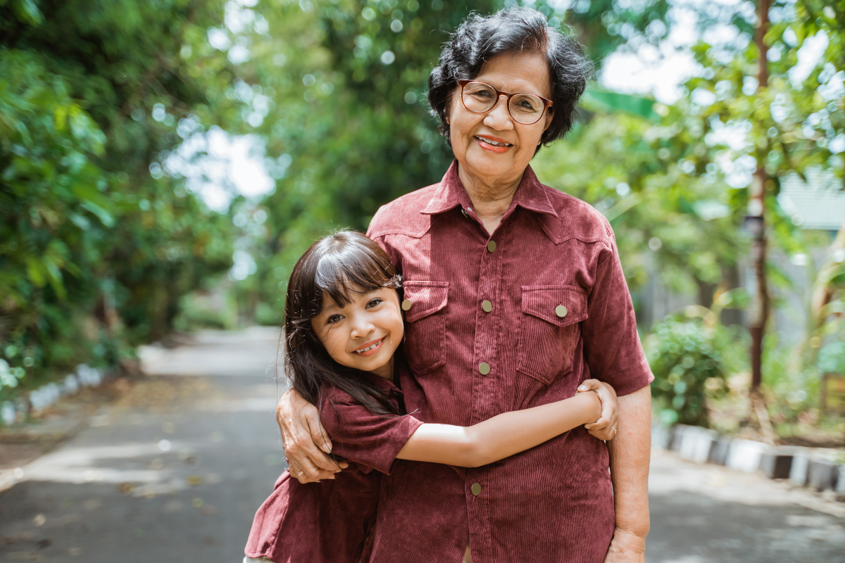 A young girl and her grandmother pose together outdoors