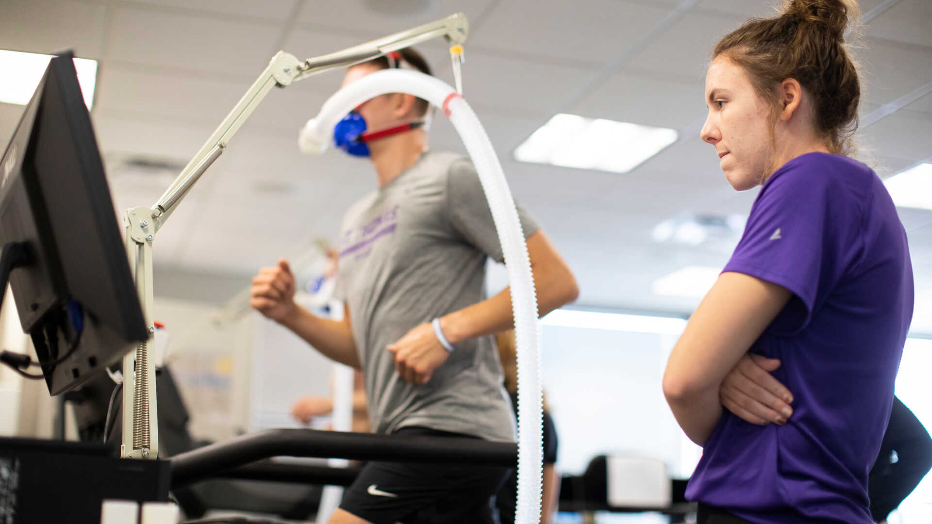 A female observes a male student running on a treadmill