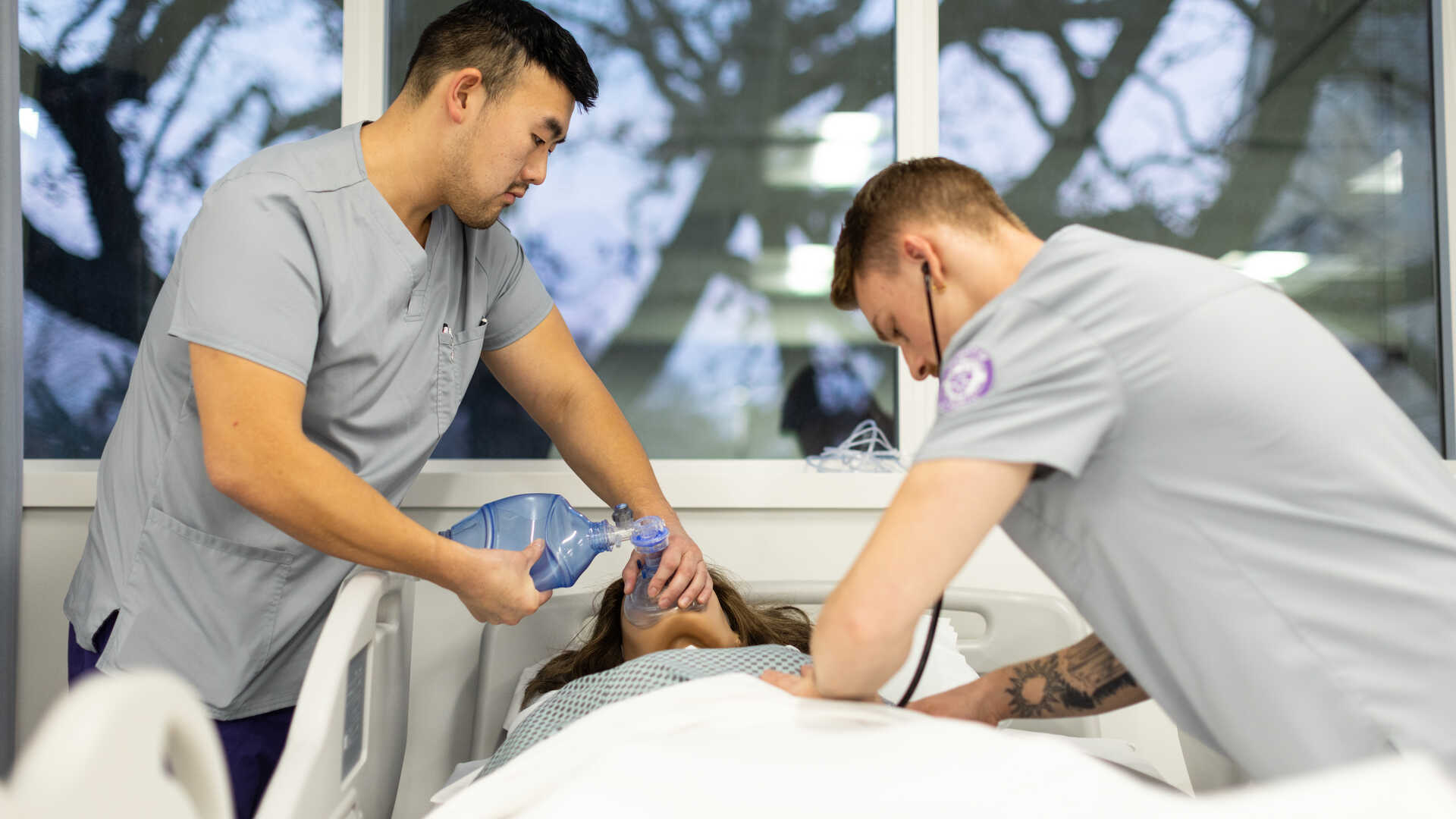 Two male nursing students working with an adult female simulation mannequin.